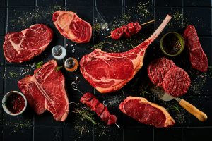 Assorted raw premium beef cuts including tomahawk steak and skewers on dark surface